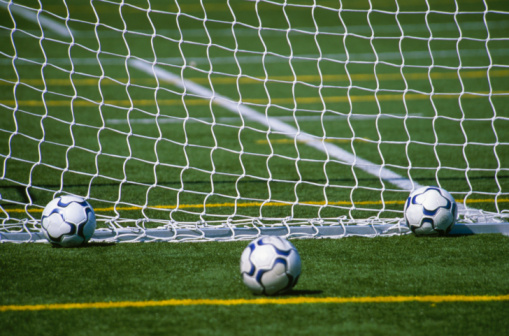 Three soccer balls behind goal net
